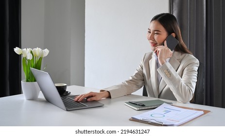 Millennial Female Financial Advisor Using Laptop And Negotiating With Client On Mobile Phone