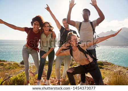 Millennial friends on a hiking trip celebrate reaching the summit and have fun posing for photos