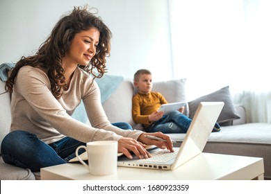 Millennial generation mother working from home with small children while in quarantine isolation during the Covid-19 health crisis. Little boy on tablet computer.  - Shutterstock ID 1680923359