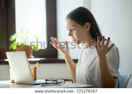 Millennial generation young adult woman looking in laptop computer, fling arms up.  She just found mistake in last assignment, error in contract, disagreement in email or dissatisfied buyer message.