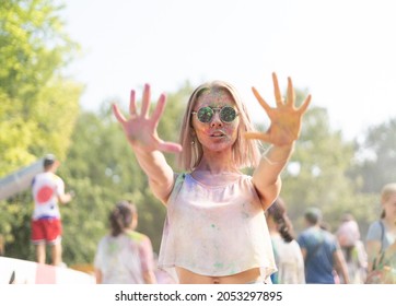 Millennial girl at the Holi Fest festival of paints in city park shows stop rocky. Traditional festival of dry urban paints. Caucasian woman in glasses with face stained with paints. - Powered by Shutterstock