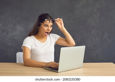 Millennial girl sit on table look at laptop screen feel shocked stunned by unexpected news online. Young Caucasian woman use computer surprised by good unbelievable sale deal or discount offer.