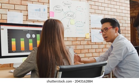 Millennial Group Of Young Asia Businessman And Businesswoman In Small Modern Urban Office. Japanese Male Boss Supervisor Teaching Intern Or New Employee Korean Girl Helping With Difficult Assignment.