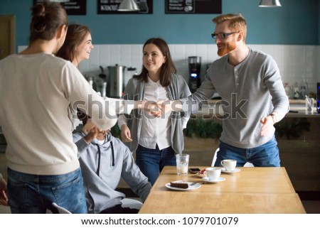 Millennial guy handshaking smiling girl introducing greeting at group meeting in cafe, happy young people get acquainted hanging together at public place, making new friends, first impression concept