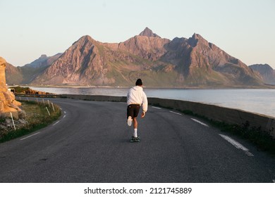 Millennial hipster skateboard away into sunset on summer evening. Young man in hoodie and shorts ride longboard in epic landscape scenery. Outdoor lifestyle vibes - Powered by Shutterstock