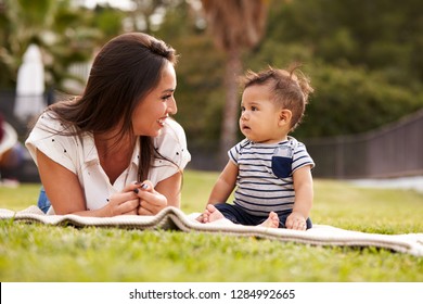 Millennial Hispanic mother lying beside her baby, sitting on a blanket in the park, close up - Powered by Shutterstock