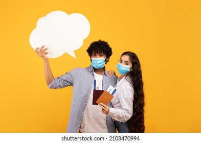 Millennial Indian Couple Wearing Face Masks, Ready To Travel Abroad During COVID-19 Pandemic, Woman Holding Passports And Flight Tickets While Man Holding Empty Speech Bubble, Yellow Background