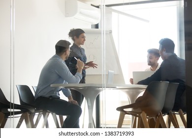 Millennial indian female speaker stand making flip chart presentation speak on company business strategy, diverse multiethnic work team brainstorm discuss share ideas meeting at briefing in office