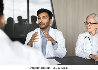 Millennial Indian male doctor speaking, sharing insights, presenting information during group seminar with colleagues, engaged in professional interaction and knowledge exchange. Medical council event - Powered by Shutterstock