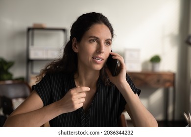 Millennial Latin Business Woman Engaged In Telephone Talk, Making Call, Speaking On Mobile Phone At Work Desk In Home Office, Consulting Customer Support Service, Looking Away, Listening