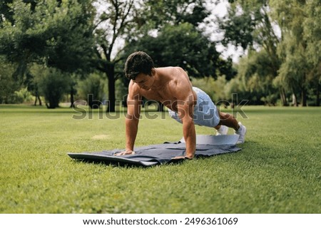 Millennial latin man doing push-ups in public park.