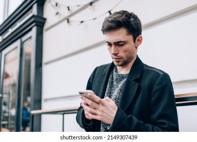 Millennial Male Blogger Checking Received Booking Confirmation On Modern Cellphone Technology, Caucasian Hipster Guy Browsing Wireless Web Page On Digital Cellular Device Using 4g Internet In City