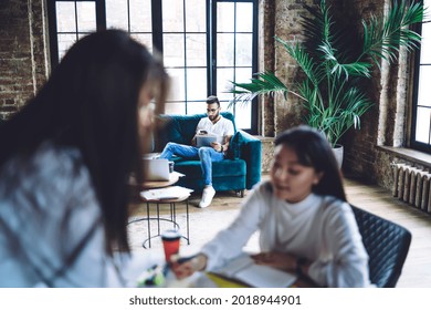 Millennial male blogger connecting to 4g wireless internet for browsing web content while blurred female on frontage discussing ideas, hipster guy using modern technology for online messaging