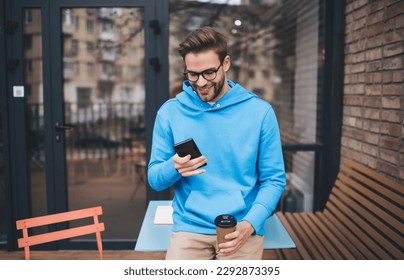 Millennial male in spectacles browsing website on modern cellphone device using 4g wireless during coffee break at street terrace, happy Caucaisan hipster guy in optical eyewear chatting and texting - Powered by Shutterstock