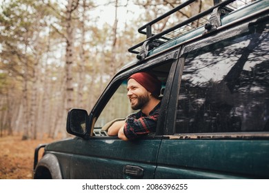 Millennial man with beard travelling off-road by car in a pine forest. Wanderlust concept.