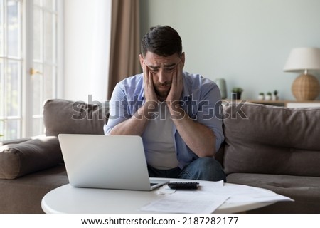 Millennial man counted income and expenses looks upset because of lack of funds for monthly mortgage payments feels desperate sit near heap of bills feels stressed. Financial failure, debts concept