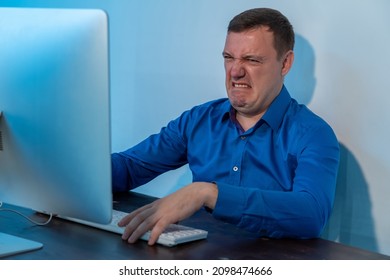 Millennial Man Looking Disgusted In Front Of His Computer In Office. Confused Businessman In Blue Shirt Cringe And Looking At Screen With Squeamishness At Startup Business Office Space