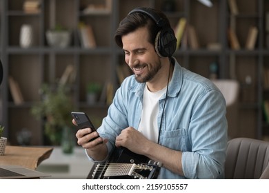 Millennial Man Musician In Headset Hold Guitar Distracted From Recording Music In Audio Editing App At Home Studio On Pc To Make Telephone Call. Smiling Young Guy Guitarist Talk On Phone By Video Call