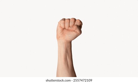 Millennial man raising his clenched fist up over light background, close up view. Panorama