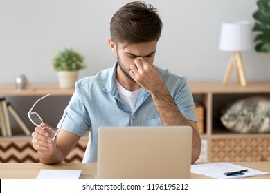 Millennial Man Sitting At The Desk In Office At Workplace Took Off Glasses Massaging His Eyes. Fatigue And Stressful Work, Poor Blurred Vision Influence Of Laptop On Human Health, Overworking Concept
