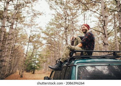 Millennial man sitting on car roof drinking beer in a pine forest. - Powered by Shutterstock