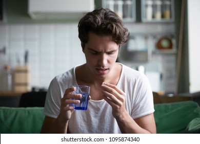 Millennial Man Taking Antibiotic Antidepressant Painkiller Pill Medication To Relieve Pain At Home, Young Guy Feeling Sick Ill Suffering From Headache, Stress Or Flu, Emergency Treatment Concept