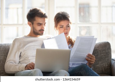 Millennial Married Couple Sitting On Couch With Computer And Documents, Reading Received Formal Letter From Bank Loan Mortgage Information, Contract Terms And Conditions Discuss Papers Working Concept