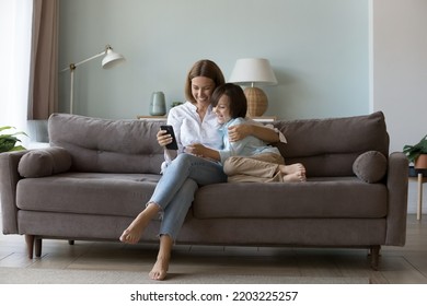 Millennial Mom Hugging Little Son On Couch, Using Online App On Mobile Phone, Talking On Video Call, Shopping On Internet, Showing Smartphone To Happy Boy. Family, Communication Concept. Full Length