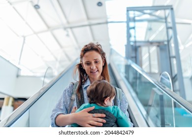 Millennial Mother Carrying Her Baby In A Shopping Area Going Down An Escalator