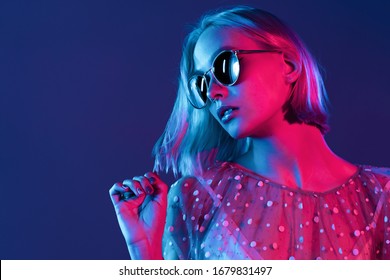 Millennial pretty girl with short hairstyle with neon light. Dyed blue and pink hair. Mysterious hipster teenager in glasses.