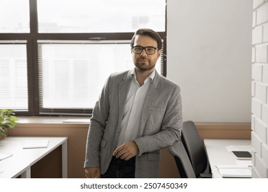 Millennial professional businessman, wearing eyeglasses and jacket standing confidently in co-working office. Financial consultant, startup entrepreneur, school teacher or department manager portrait - Powered by Shutterstock