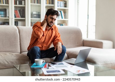 Millennial tired stressed middle eastern man having neck pain, touching massaging neck sitting on couch, working on laptop at home, suffering from discomfort long hours of sedentary, overworking - Powered by Shutterstock