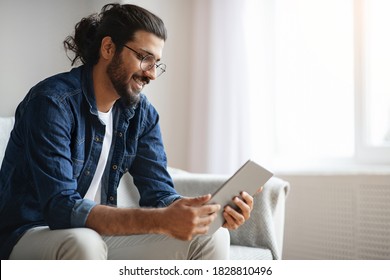 Millennial Western Guy Spending Time With Digital Tablet At Home, Reading News, Browsing Internet, Watching Videos, Checking Social Networks While Relaxing On Couch In Living Room, Copy Space