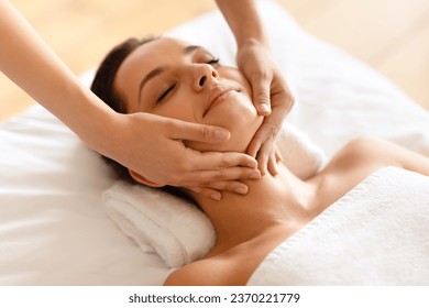 Millennial woman enjoying face building massage, lying with eyes closed while professional therapist making skin lift procedure indoor, high angle shot, closeup. Beauty treatment and spa - Powered by Shutterstock