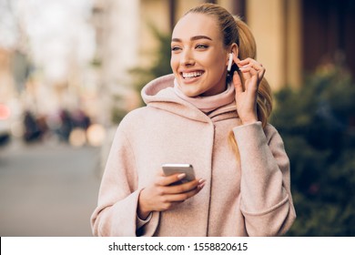 Millennial woman enjoying music in airpods, walking in city on weekend