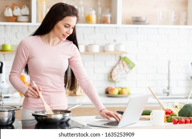 Millennial Woman In Kitchen Cooking With Reference The Laptop, Empty Space