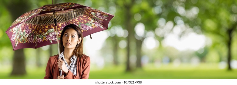 Millennial woman with patterned umbrella against blurry green trees - Powered by Shutterstock