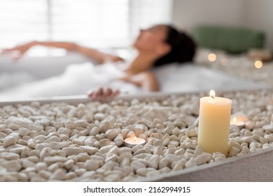 Millennial woman relaxing in bathtub with foam, having spa day at home, selective focus on candles and pebbles. Young lady having lazy weekend, enjoying hot bubble bath at hotel, empty space - Powered by Shutterstock