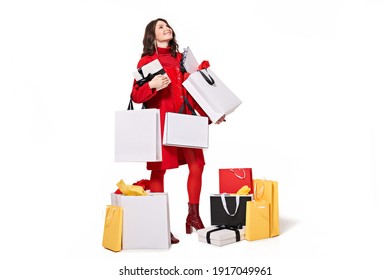 Millennial woman shopper holding shopping bags while looking up. Pretty woman shopaholic standing over white studio background and holding paper bags with purchases. Shopping concept