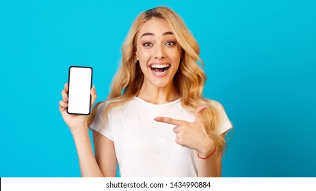 Millennial Woman Showing Phone With Blank Screen And Pointing On It, Blue Background