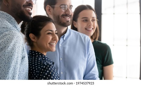 Millennial workers of different races celebrating accomplished project. Diverse happy employees standing together. Indian female business leader smiling and posing with colleagues. Candid shot