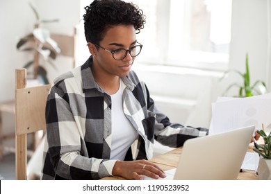Millennial young african employee in eyeglasses hold documents papers with charts and graphics using computer sitting at the desk in office room or home feels confident, fruitful working day concept - Shutterstock ID 1190523952