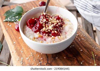 Millet Breakfast Porridge With Sour Cherry Compote And Roasted Nuts In A Bowl.