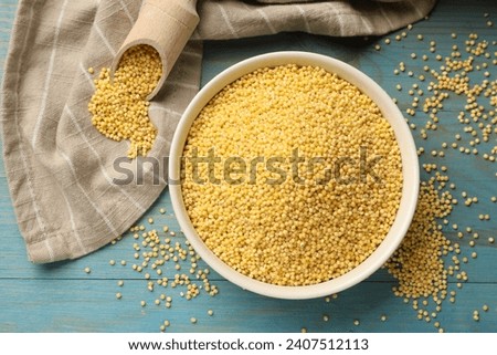 Millet groats in bowl and scoop on light blue wooden table, flat lay