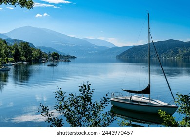 Millstatt am See, Kärnten - Austria - 06-16-2021: Millstätter Lake: An anchored sailboat floats on a tranquil Austrian lake, framed by alpine mountains - Powered by Shutterstock