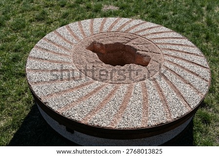 Millstone with grooves and textured surface resting outdoors on green grass