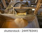 A millstone is spinning. A stone grinds grain in a mill. Production of corn flour. Corn kernels fall into the mill. Traditional watermill on the river.