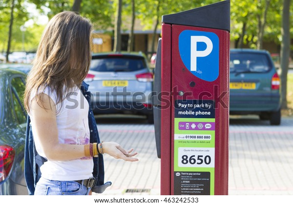 MILTON\
KEYNES, ENGLAND - JULY 27, 2016: Female customer paying for parking\
the car using installed machine outdoors,\
UK