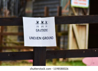 Milton Keynes, UK - 22 August 2018: A Caution Uneven Ground Sign On A Wooden Fence With A Sheep In A Farm Car Park.