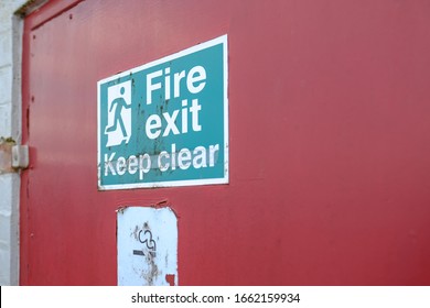 Milton Keynes, UK - Circa March 2020: Shallow Focus Of An Old Fire Exit And No Smoking Sign Seen Attached For A Fire Door, Used For Emergency Exit For A Warehouse And Logistics Company.